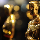 An Oscar statue against a black and gold bokeh background; additional statuettes are in the back, although they are out of focus.